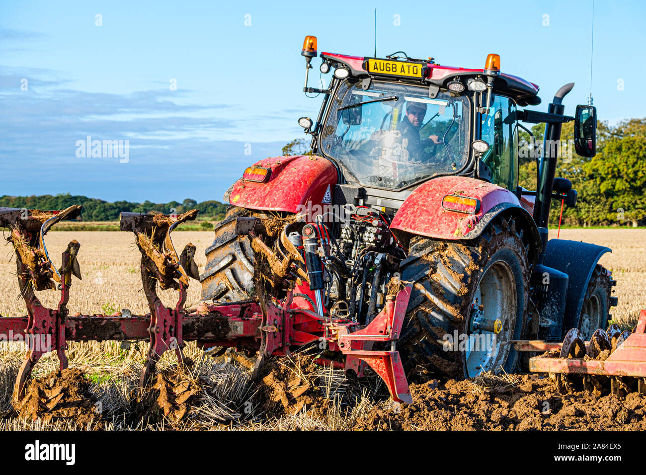 A tractor pulls a plough and press cultivator across a field in autumn ready for seeding. Stock Photo
