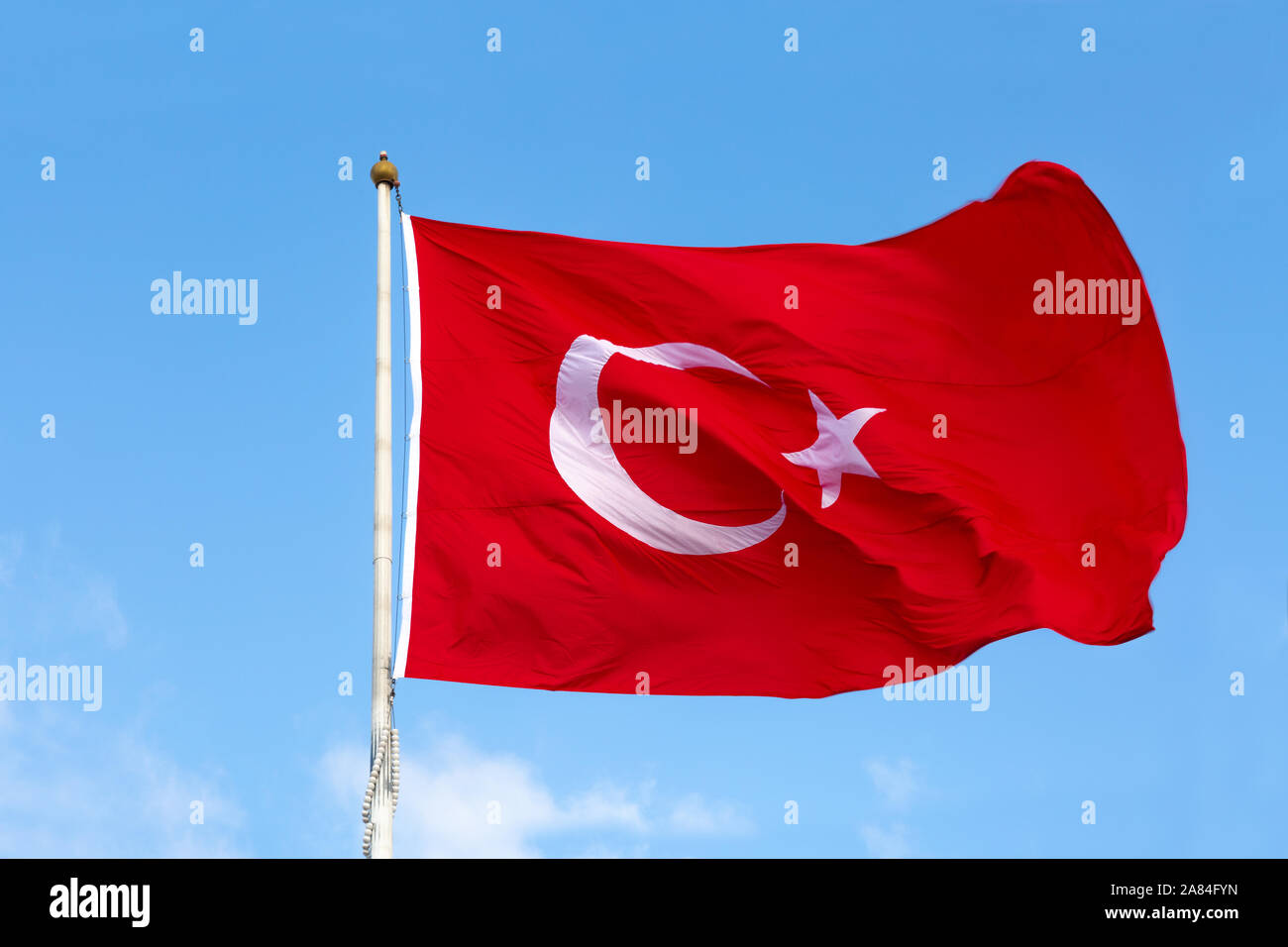 Waving Turkish Flag with clear blue sky in the background on a sunny day . Turkish flag consists of a crescent and a star inside it with red color. Stock Photo