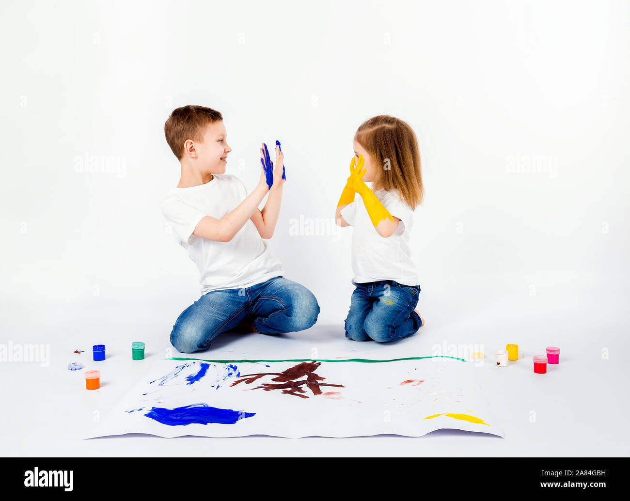 Two Pretty Child Friends Boy And Girl In White Shirts And Blue Jeans Trendy Hair Style Barefoot Drawing Pictures On White Sheet Of Paper By Paints Isolated On White Shaking Hands Stock Two Pretty Child Friends Boy And Girl In White Shirts And Blue Jeans Trendy Hair Style Barefoot Drawing Pictures On White Sheet Of Paper By Paints Isolated On White Shaking Hands Stock
