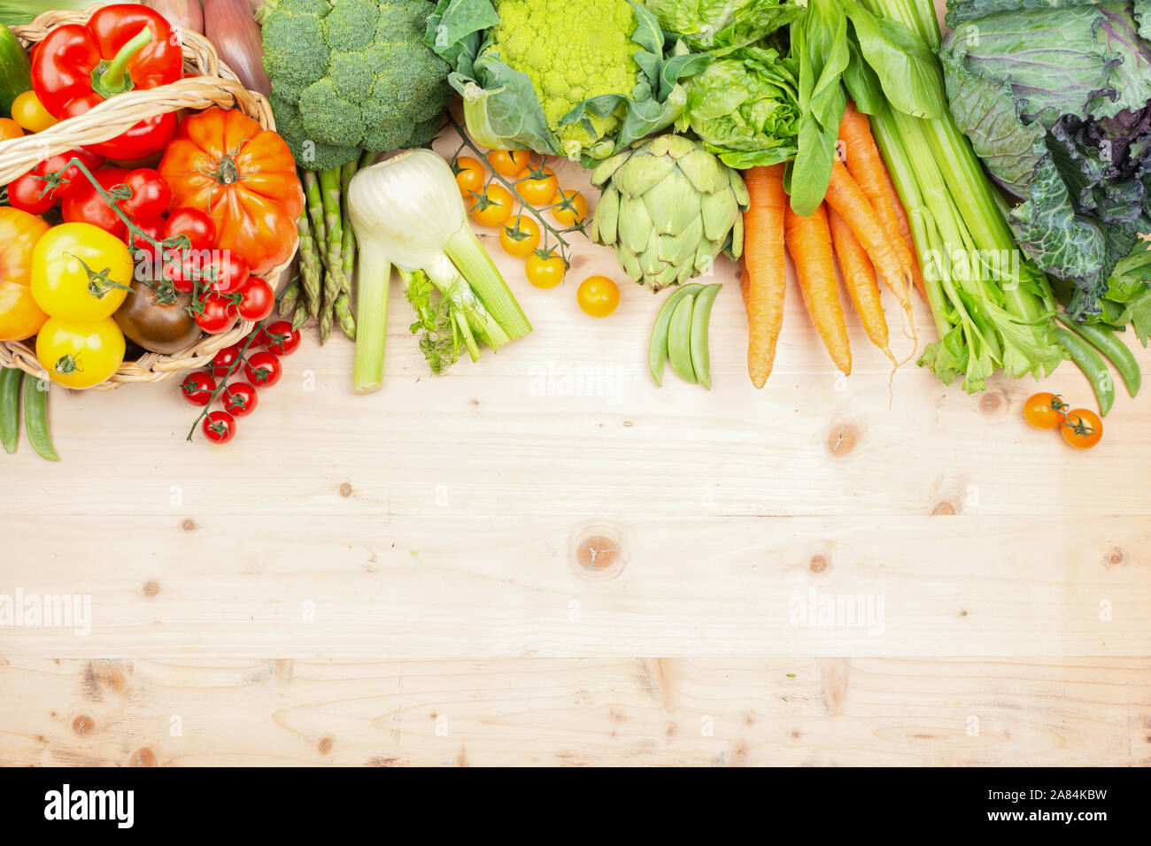 Top view of vegetables on wooden table and wicker basket, carrots velery tomatoes cabbage broccoli, copy space, selective focus Stock Photo