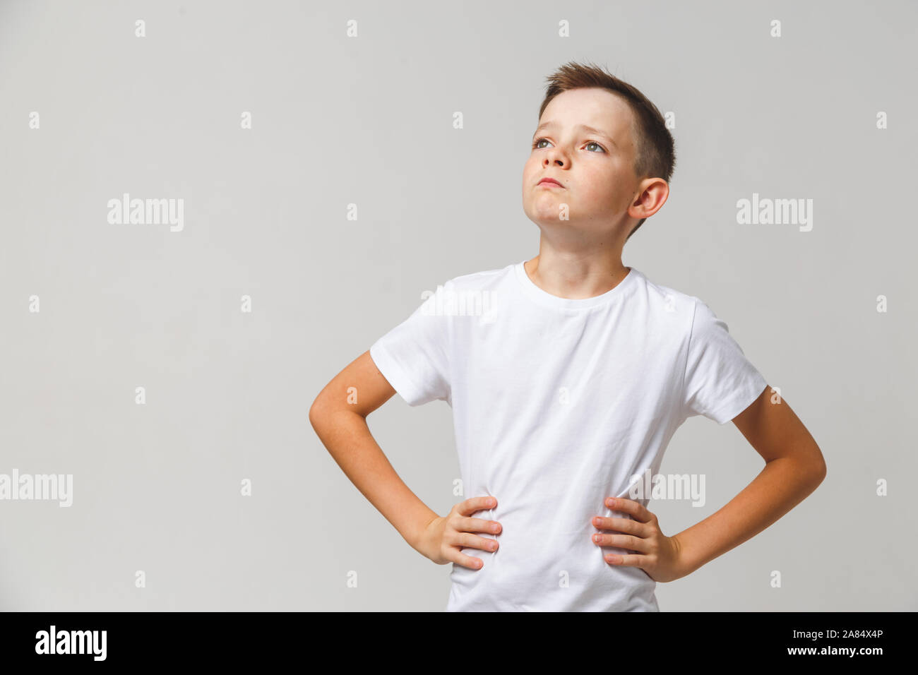 Portrait of young boy with hands on his waist lifting his head on white background Stock Photo