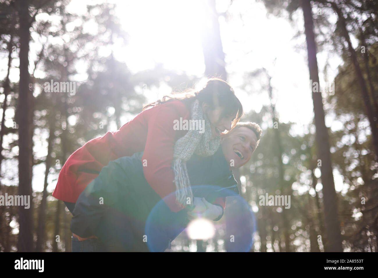 Happy, playful couple piggybacking in sunny, autumn woods Stock Photo