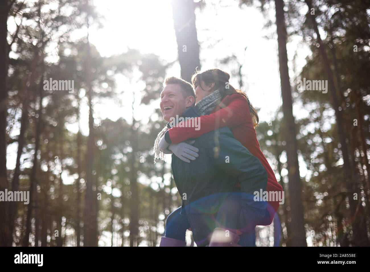 Happy, playful couple piggybacking in sunny woods Stock Photo