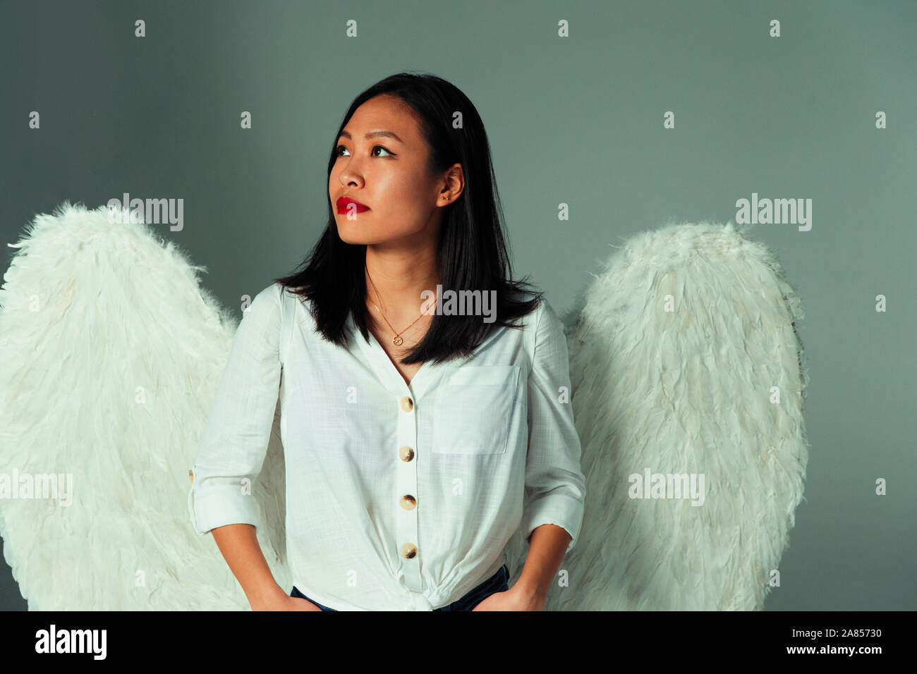 Serene, curious young woman wearing angel wings Stock Photo