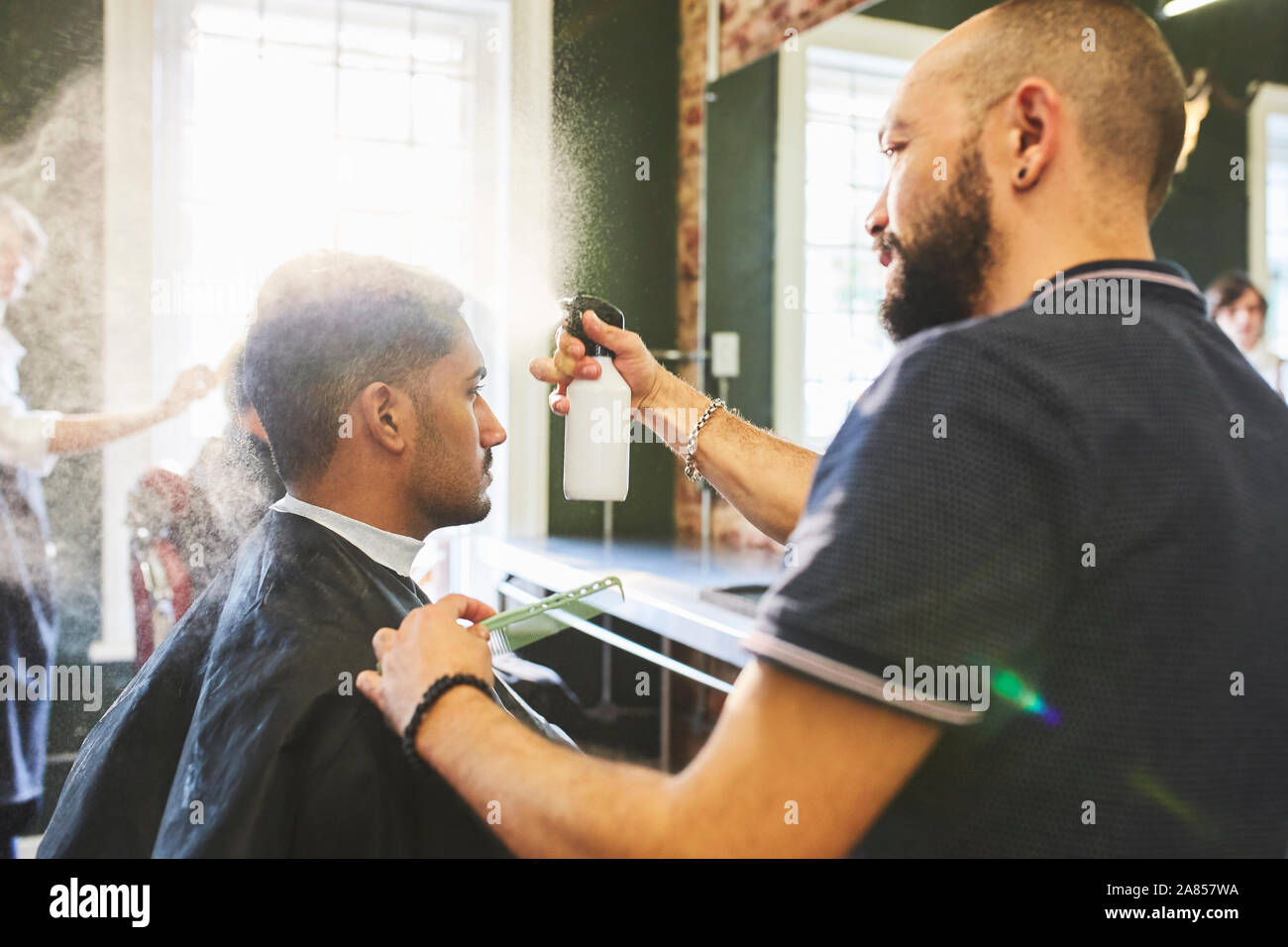 Male barber spraying hair of man in barbershop Stock Photo