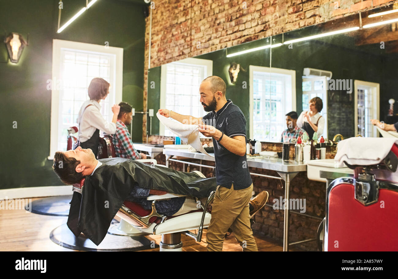 Male barber preparing to steam face of customer before shave in barbershop Stock Photo