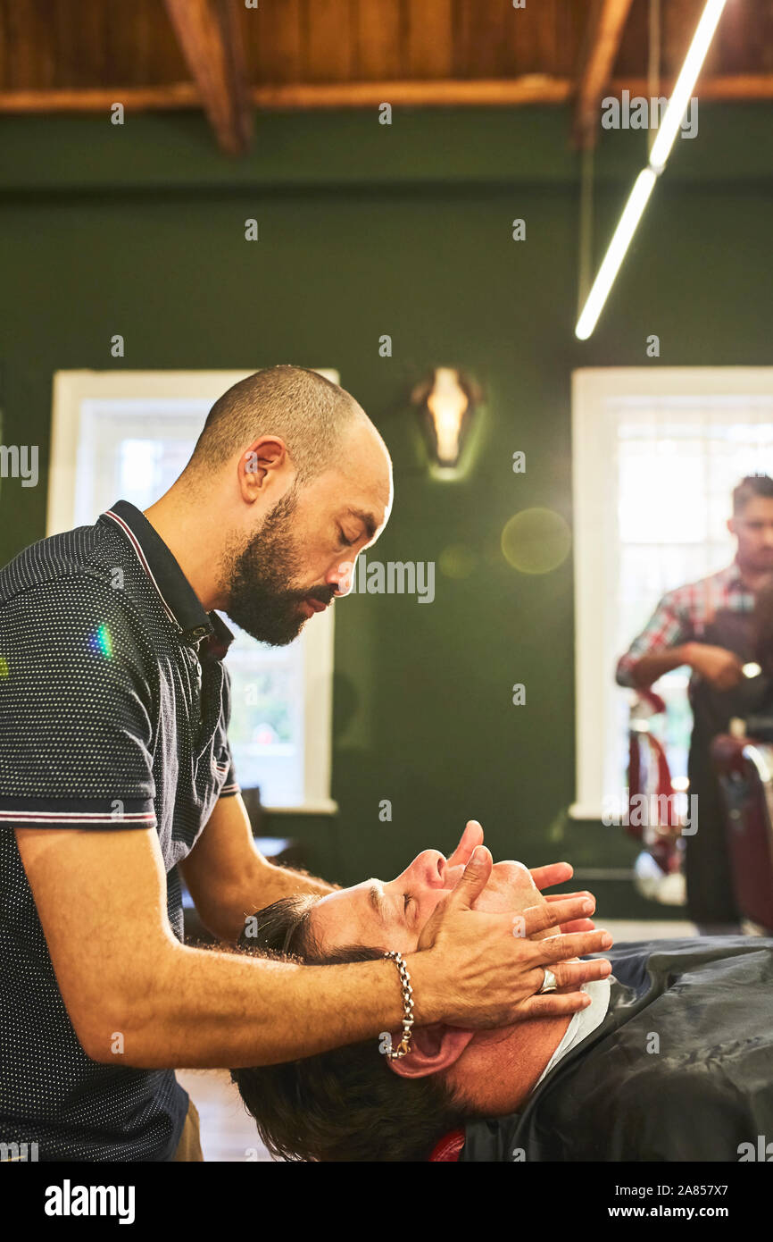 Male barber massaging face of customer in barbershop Stock Photo
