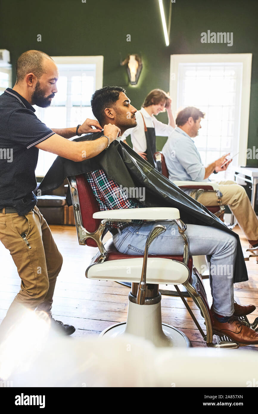 Male barber preparing customer for haircut in barbershop Stock Photo