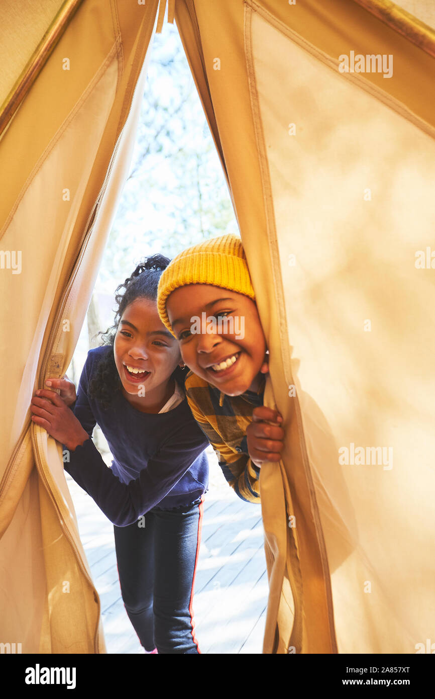 Playful brother and sister peeking into camping teepee Stock Photo