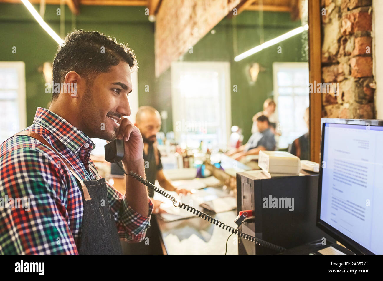 Male barber talking on telephone at computer in barbershop Stock Photo