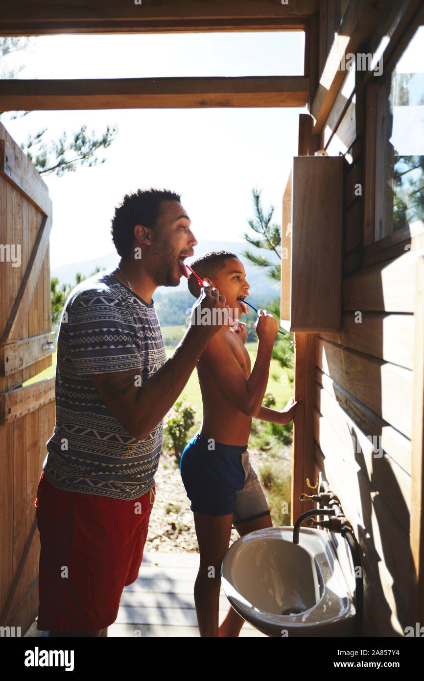 Father and son brushing teeth at sunny campsite bathroom mirror Stock Photo