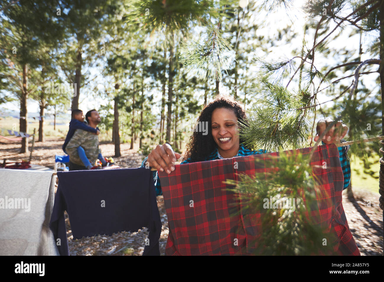 Smiling woman hanging clothing on campsite clothesline in woods Stock Photo