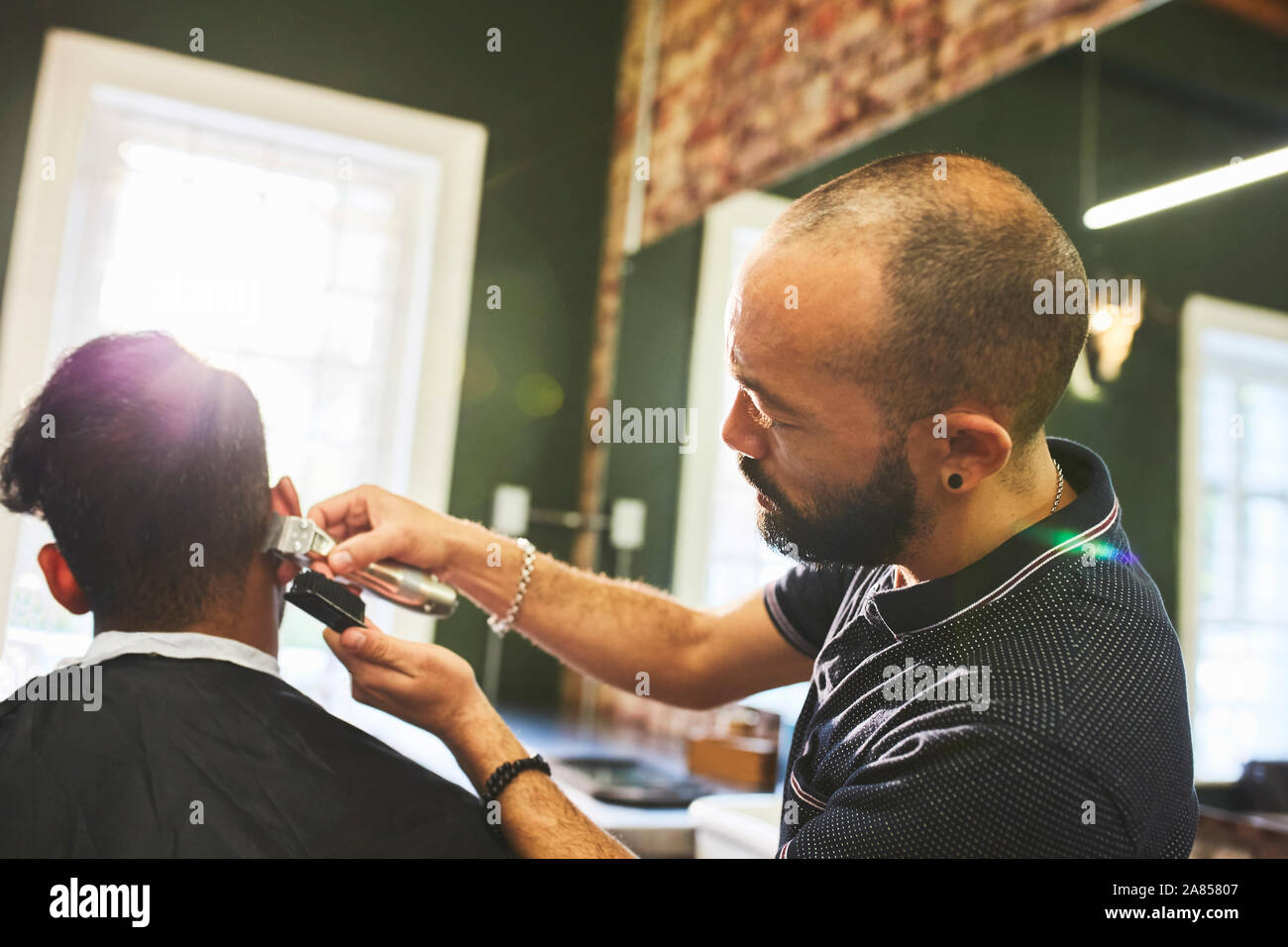 Male barber with trimmers giving customer haircut in barbershop Stock Photo