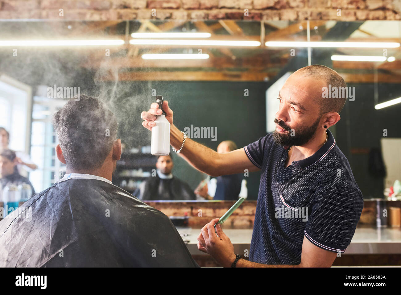 Male barber spraying hair of customer in barbershop Stock Photo