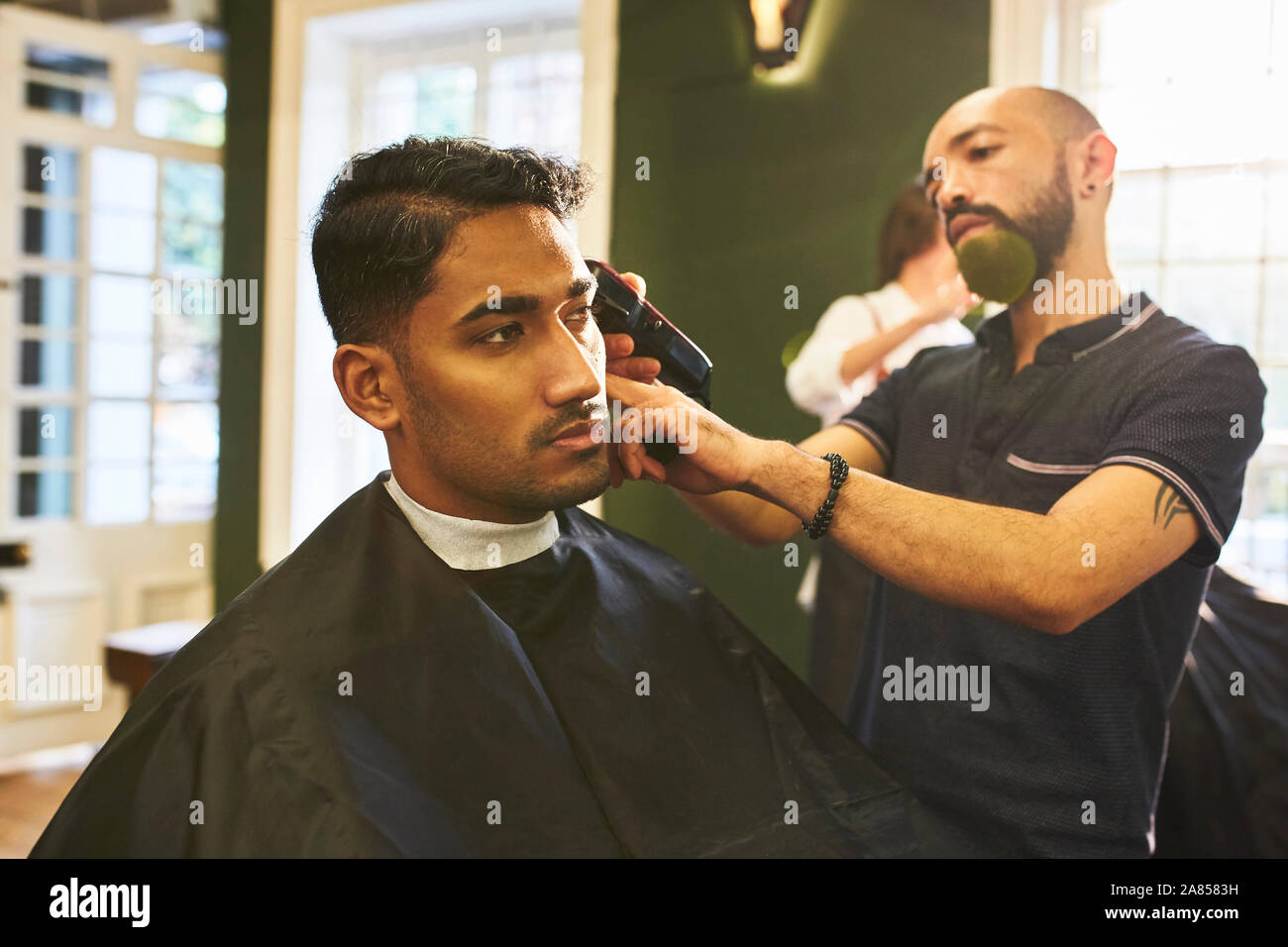 Male barber shaving hair of customer in barbershop Stock Photo