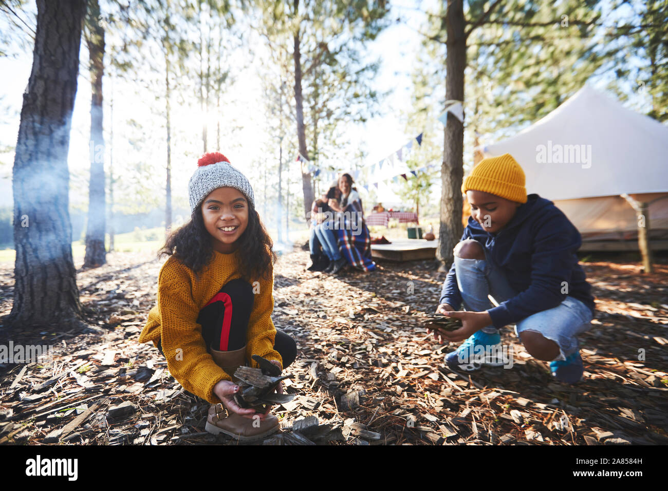 Portrait smiling girl gathering kindling at sunny campsite in woods Stock Photo