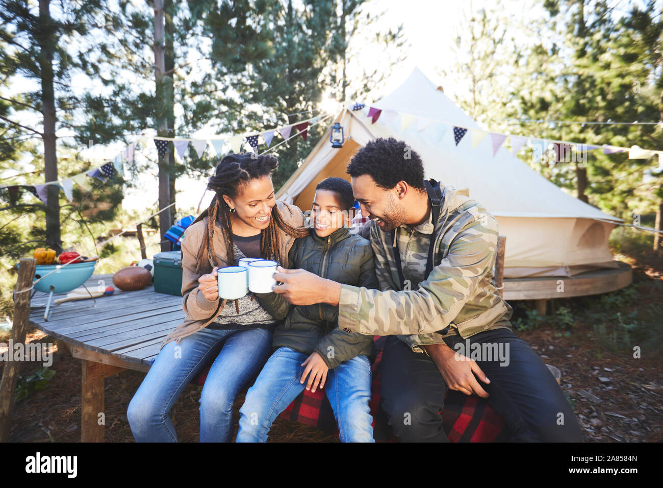 Happy family drinking coffee and hot chocolate at campsite in woods Stock Photo