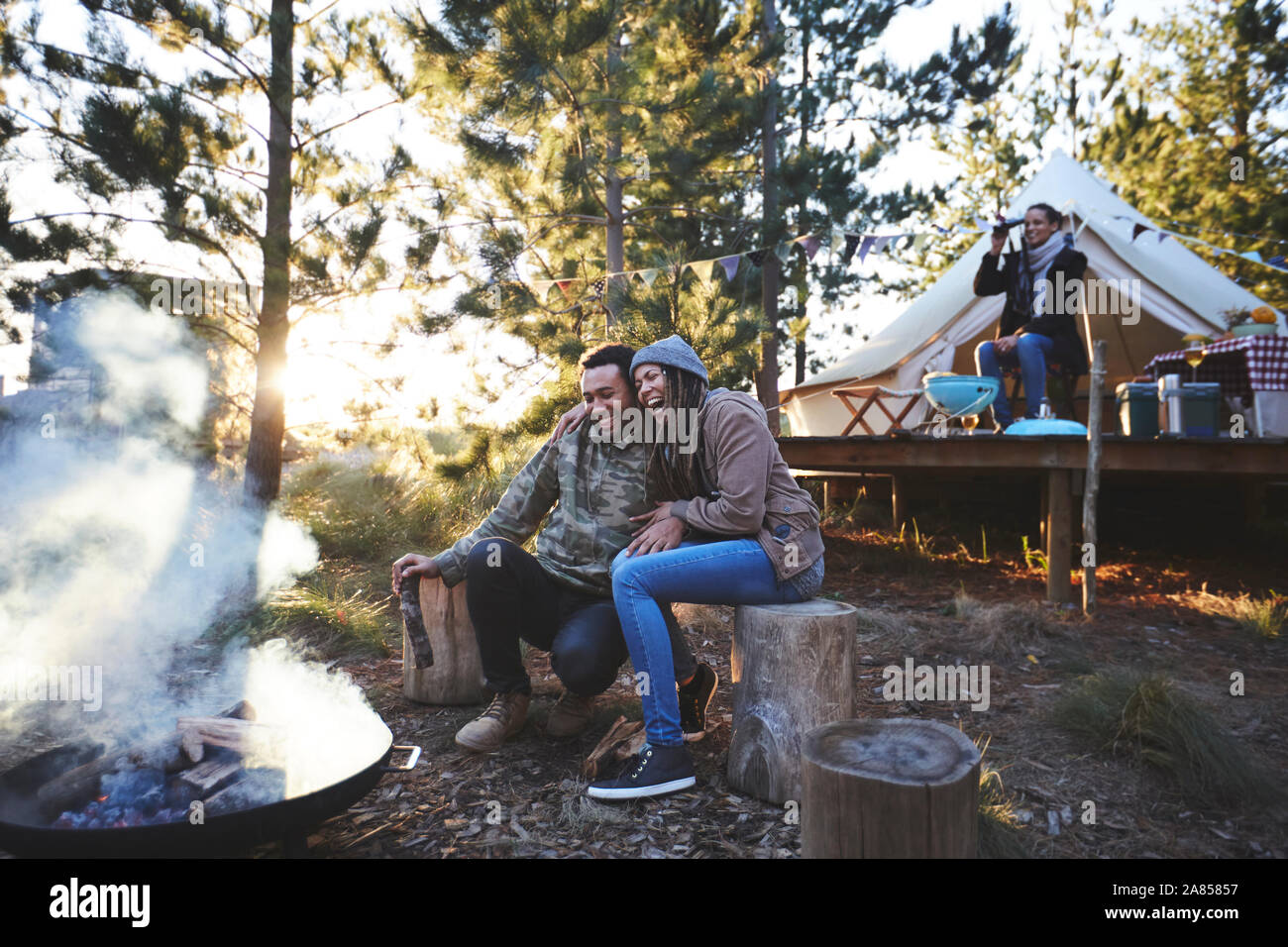 Happy couple sitting at campsite campfire in woods Stock Photo