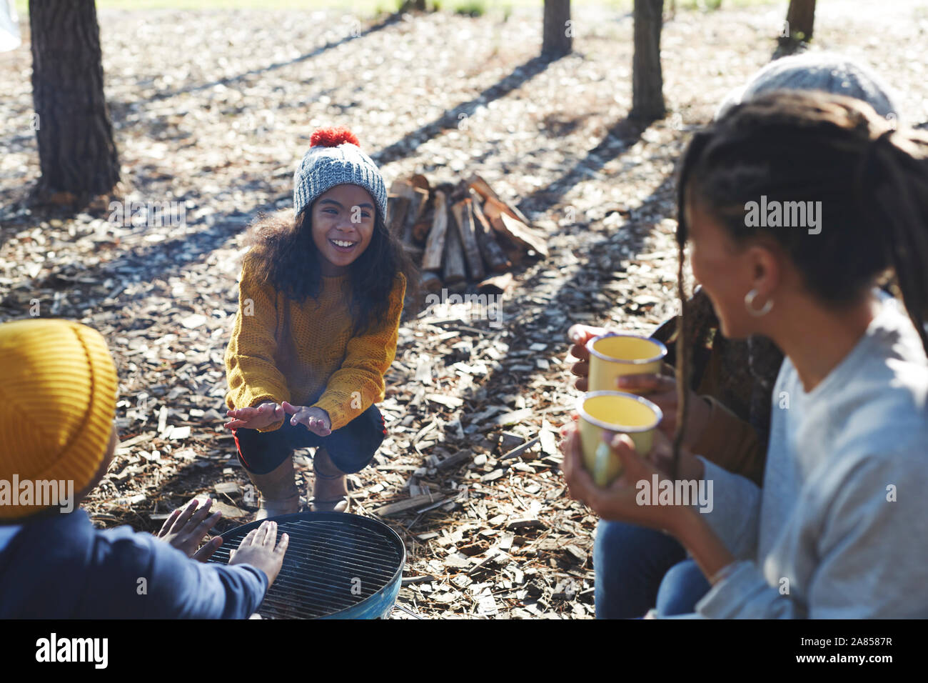 Happy family relaxing around camping grill at sunny campsite Stock Photo