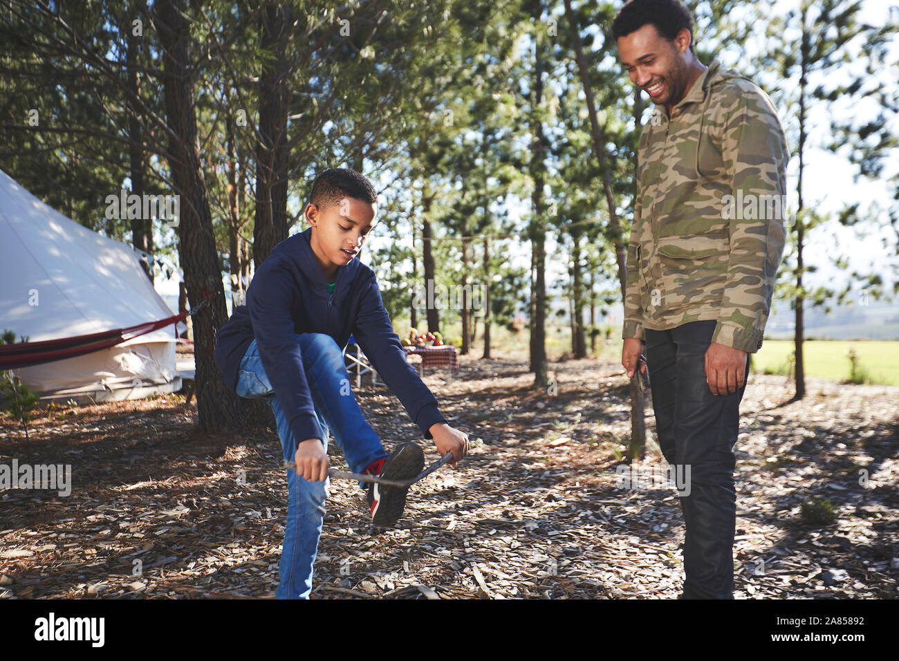 Father watching son breaking kindling at campsite in woods Stock Photo