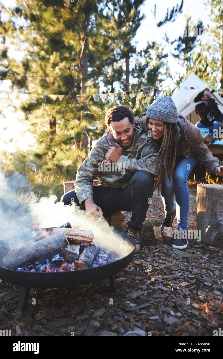 Happy couple tending to campfire at campsite in woods Stock Photo