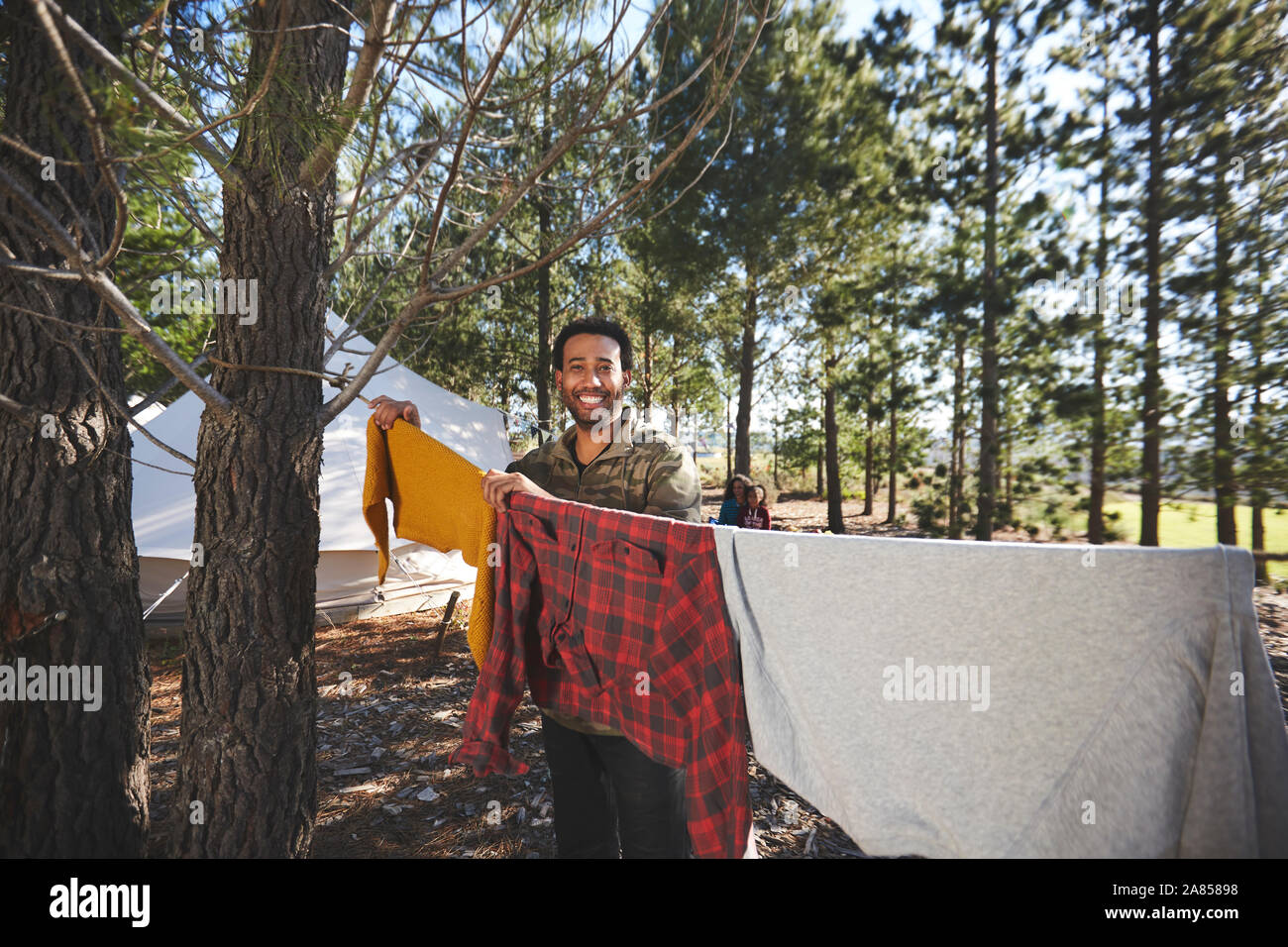 Portrait happy man hanging laundry on campsite clothesline n woods Stock Photo