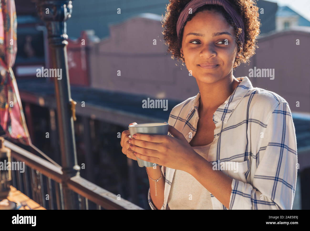 Smiling young woman drinking coffee on sunny balcony Stock Photo