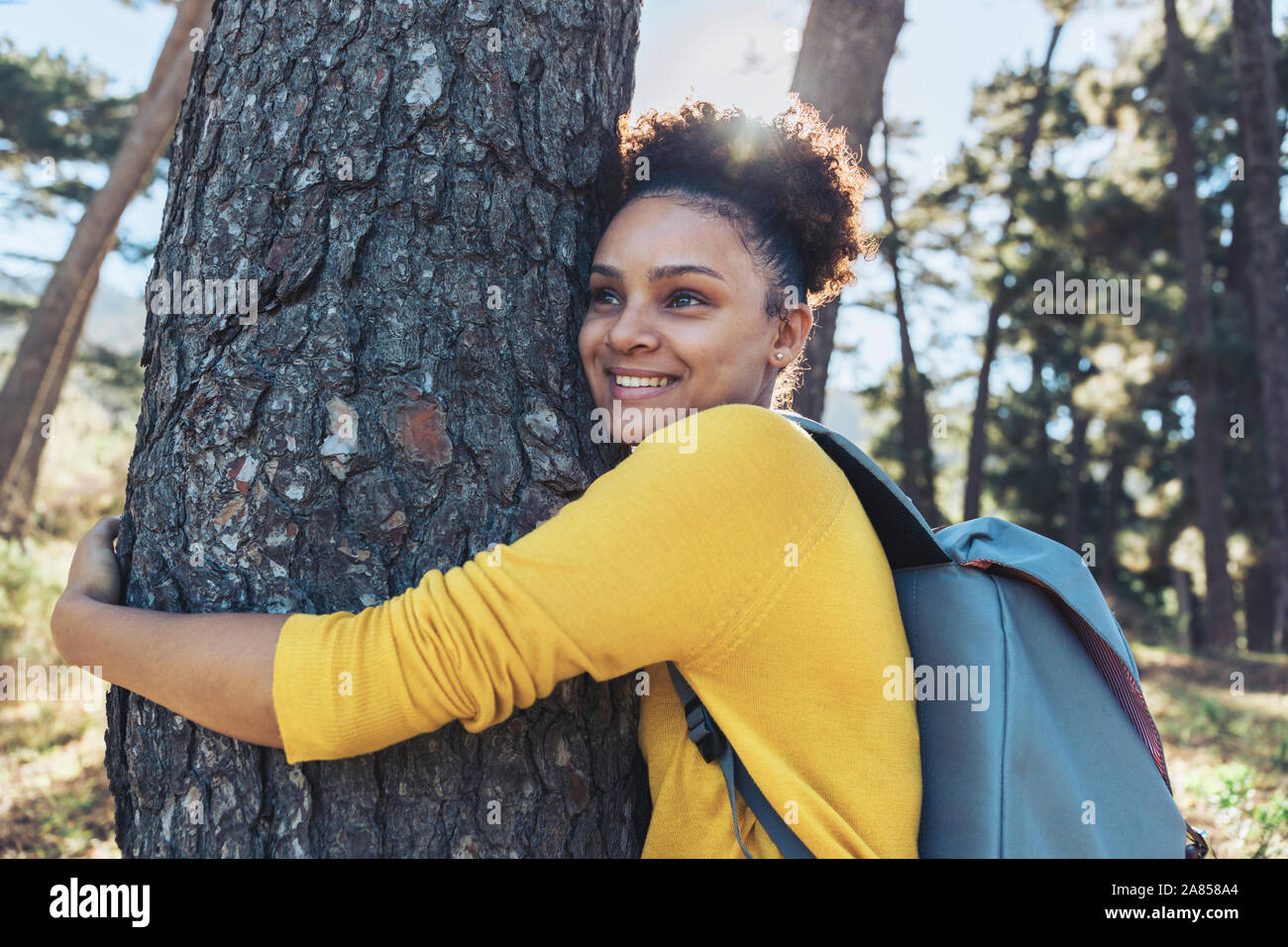 Happy, carefree young female hiker hugging tree in sunny woods Stock Photo