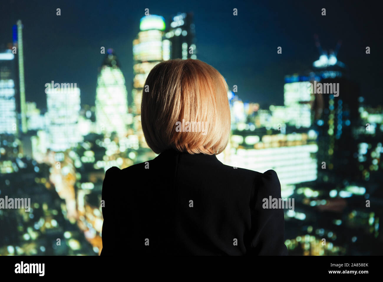 Businesswoman looking out at bright cityscape lights Stock Photo