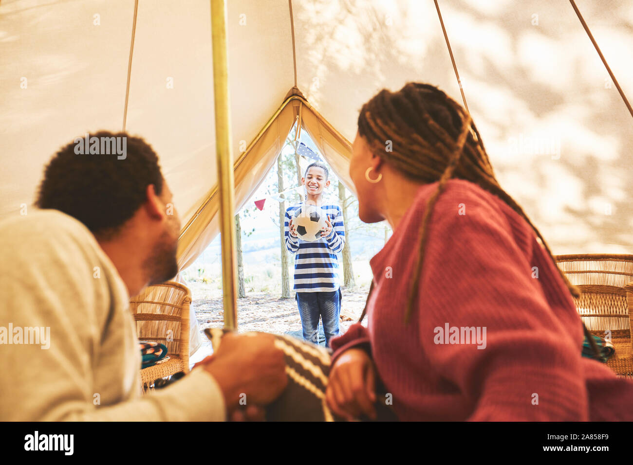 Couple watching son with soccer ball at camping yurt doorway Stock Photo