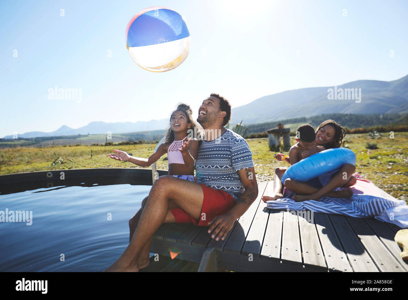 Playful family with beach ball at sunny, summer swimming pool Stock Photo