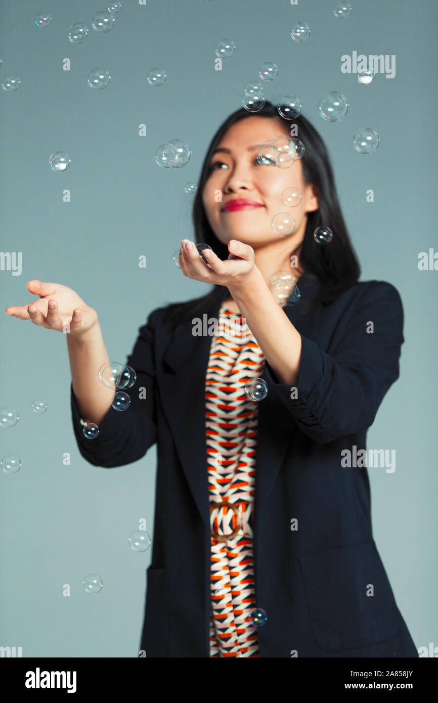 Smiling, carefree businesswoman catching falling bubbles Stock Photo