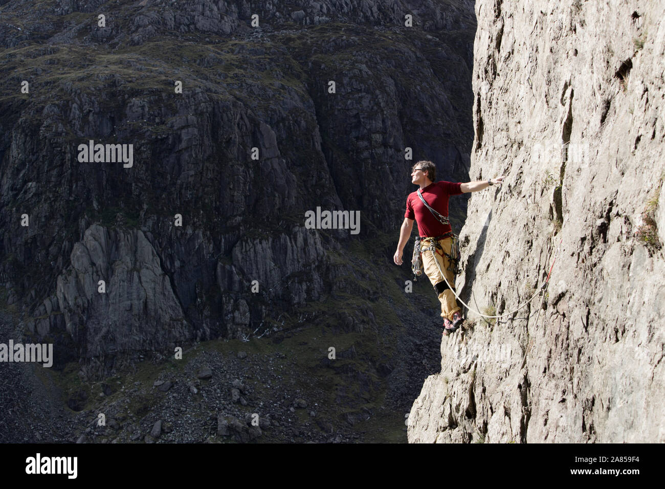 Male rock climber scaling tall rock face, looking at view over shoulder Stock Photo