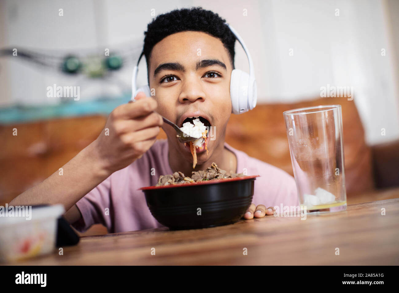 Portrait teenage boy with headphones eating at coffee table Stock Photo