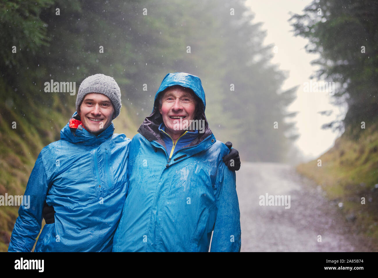 Portrait happy father and son hiking on trail in rainy woods Stock Photo
