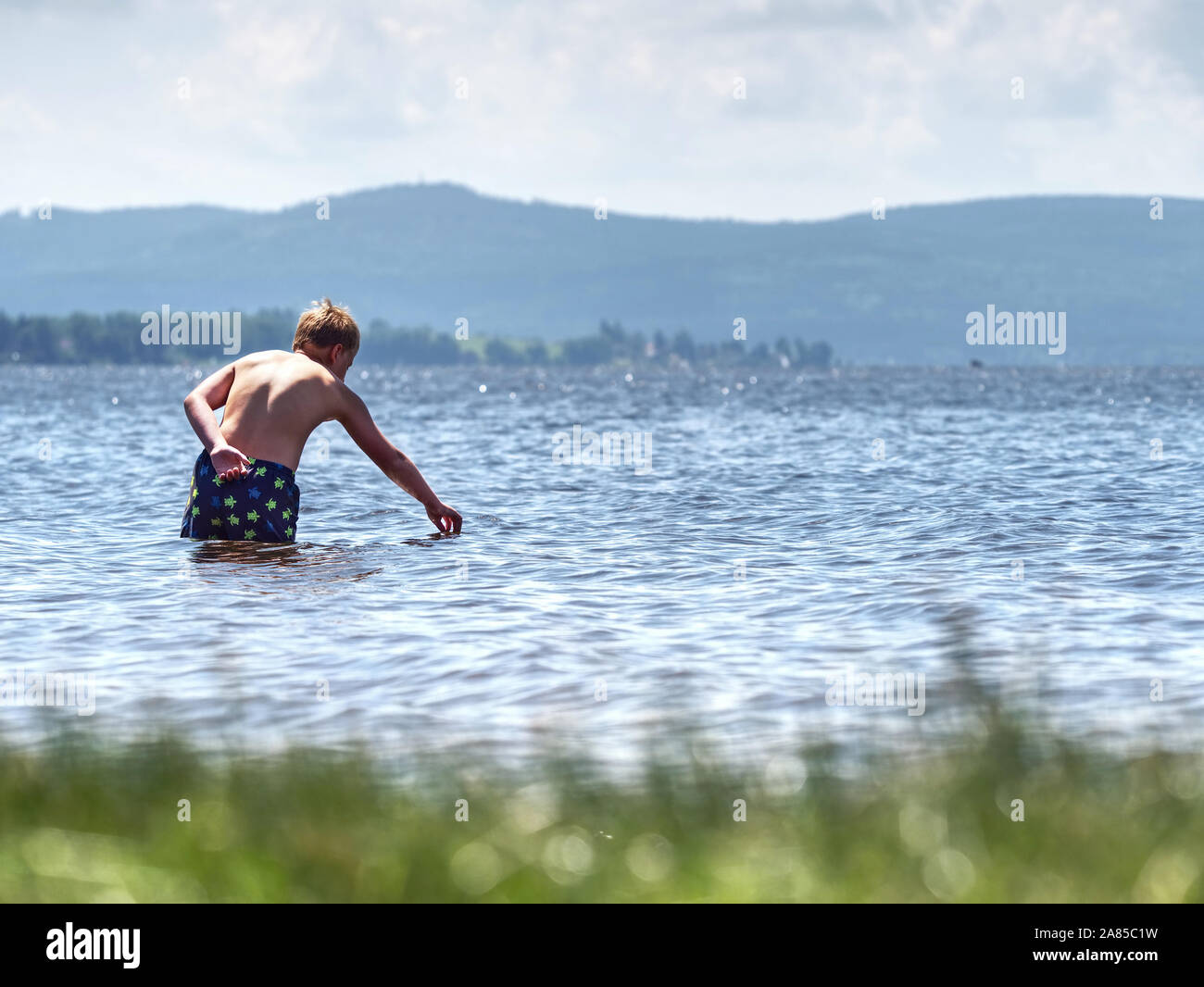 Boy stay in cold lake with water under knee and test temperature. Cold