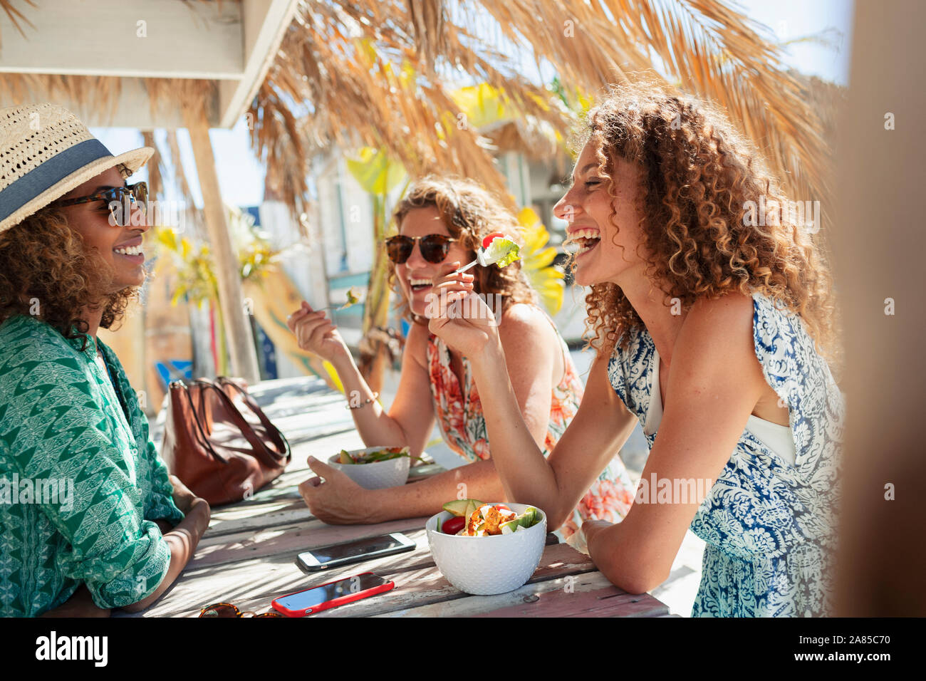 Happy women friends eating salad at sunny beach bar Stock Photo