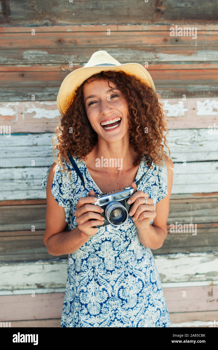 Portrait happy, carefree young woman with retro camera against wood plank wall Stock Photo