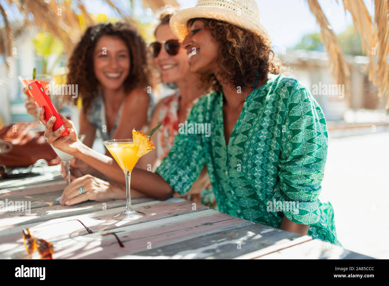 Happy women friends using smart phone and drinking cocktails at sunny beach bar Stock Photo