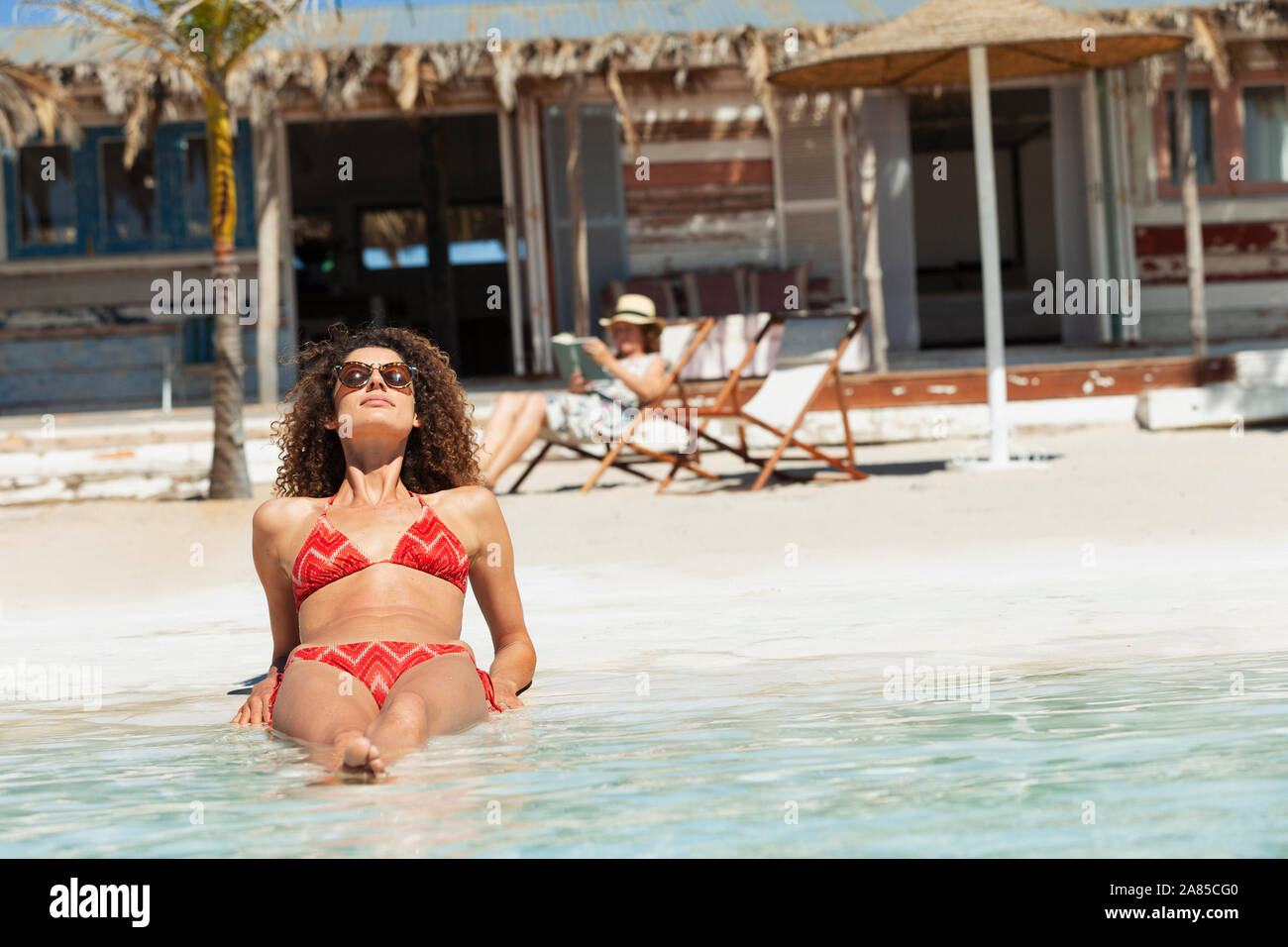 Serene young woman in bikini sunbathing on sunny beach Stock Photo