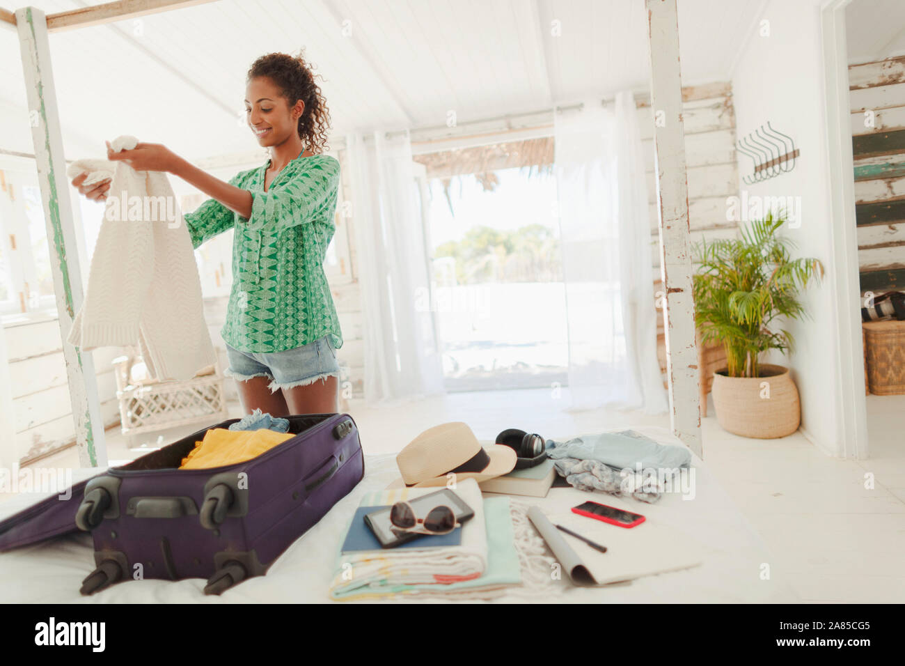 Young woman unpacking suitcase on beach hut bed Stock Photo
