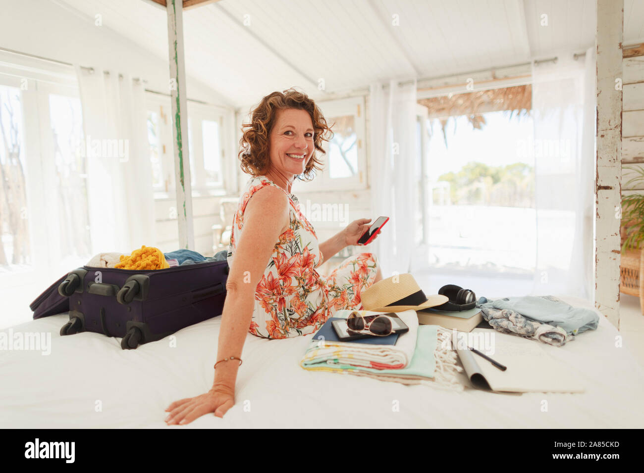 Portrait happy woman unpacking suitcase on beach house bed Stock Photo