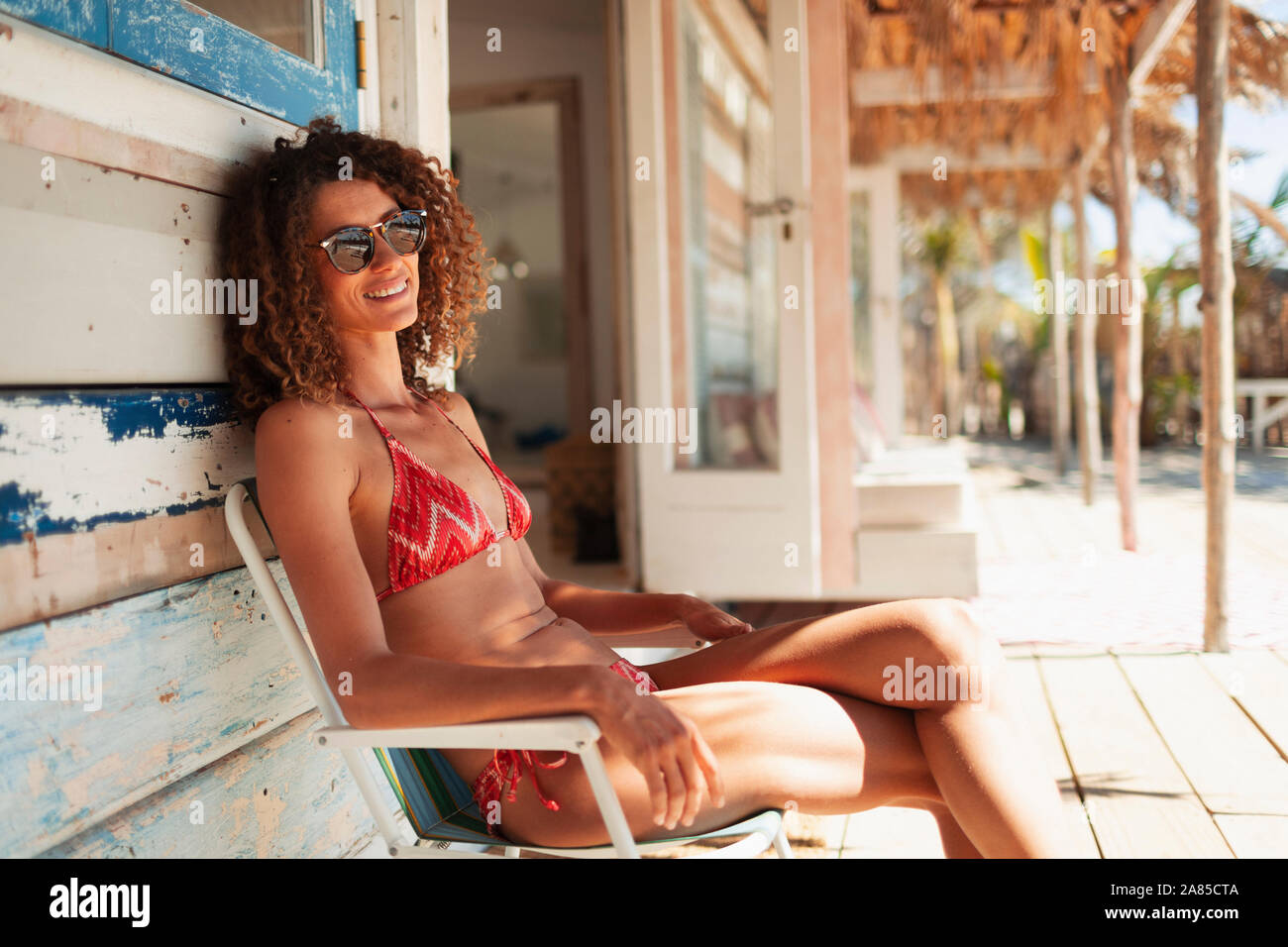 Portrait carefree young woman in bikini relaxing on beach hut patio Stock Photo