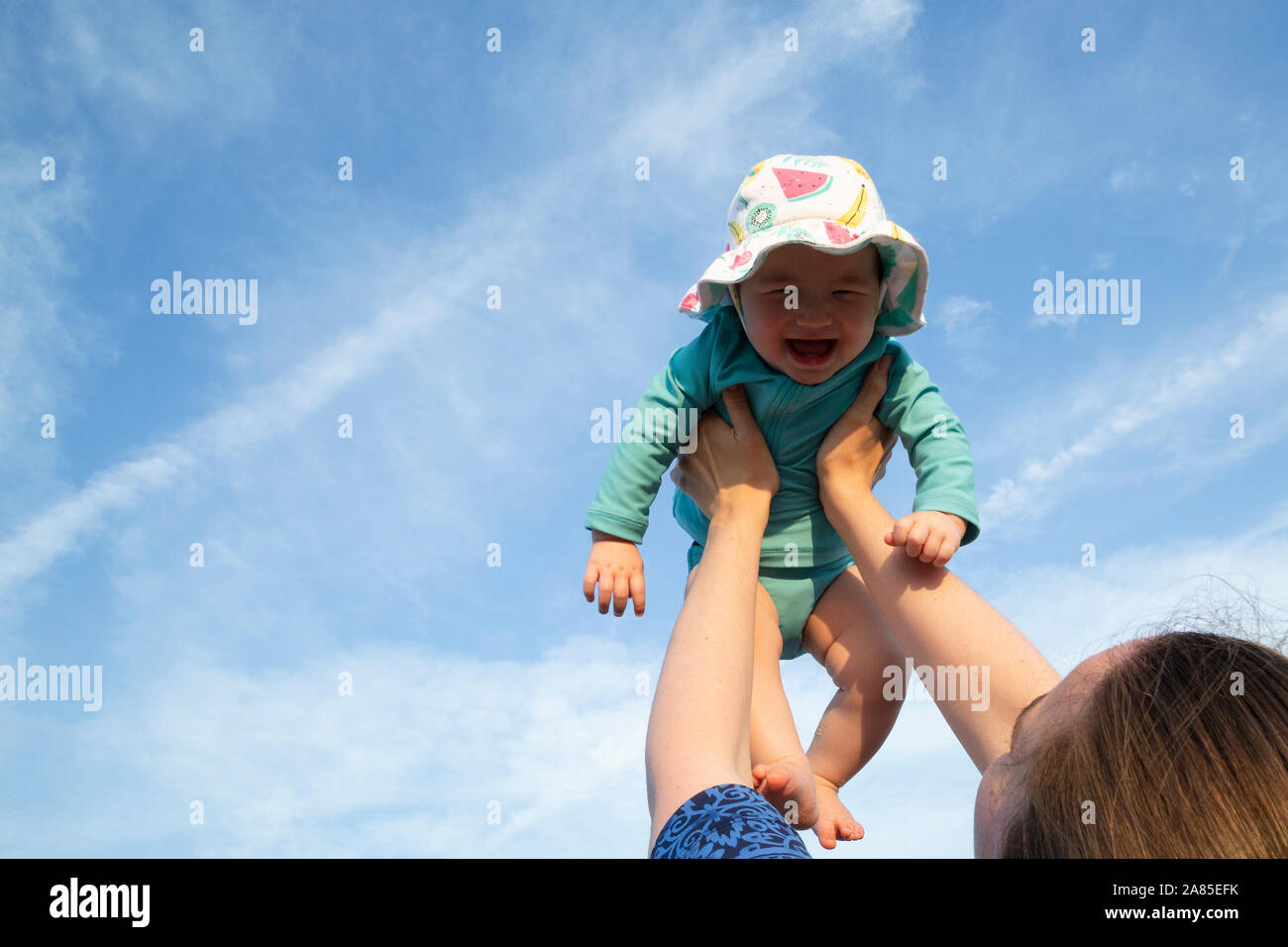 Mother holding baby girl up in air with both arms against a blue sky Stock Photo