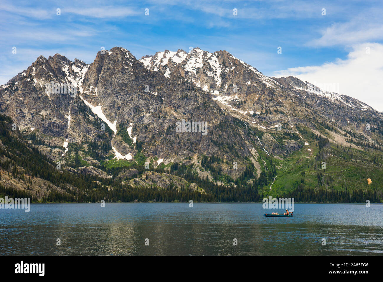Person in a canoe fishing in Jenny Lake, mountains behind Stock Photo