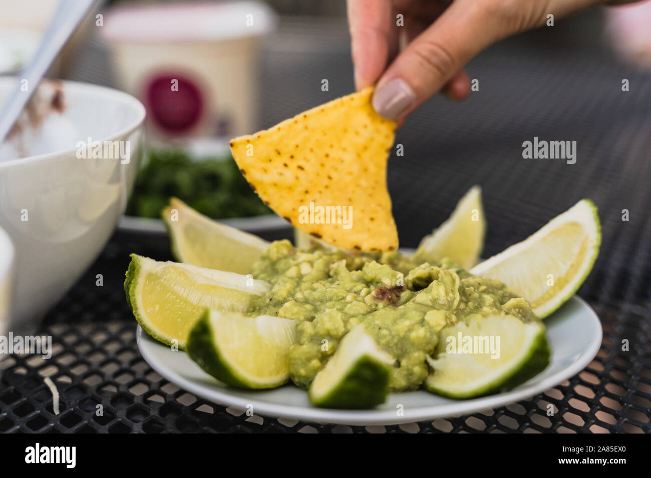 Tortilla dipping into smashed avocado, green guacamole dip Stock Photo