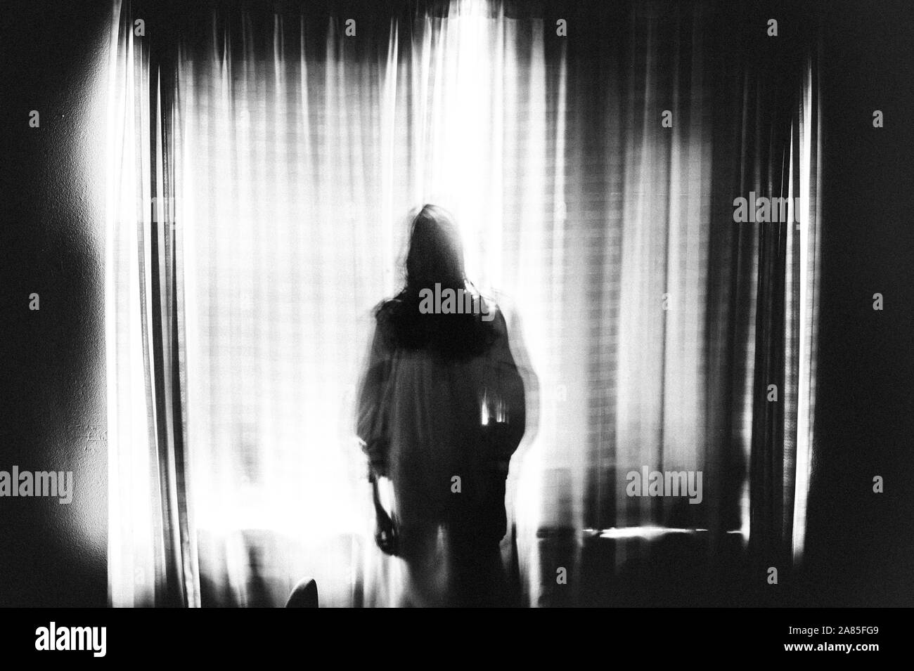 Spooky image of ghost girl standing in window in eery light Stock Photo