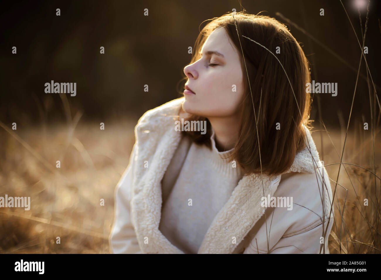 Beautiful woman sitting on soft dry grass during sunset. Stock Photo