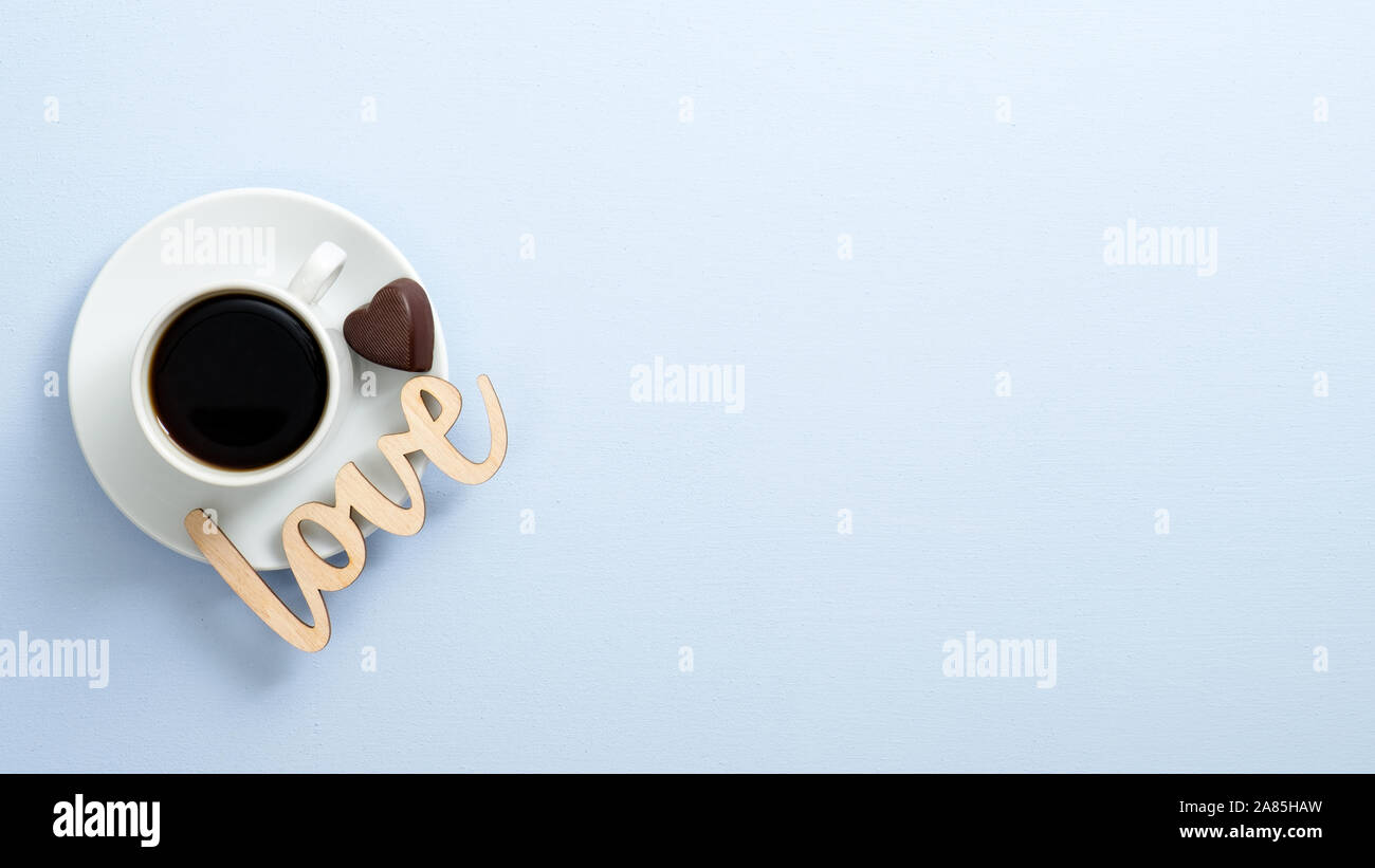 Top view coffee cup espresso with heart shaped chocolate candy and wooden word sign 'Love' on blue background. Flat lay, overhead. Valentine's day con Stock Photo