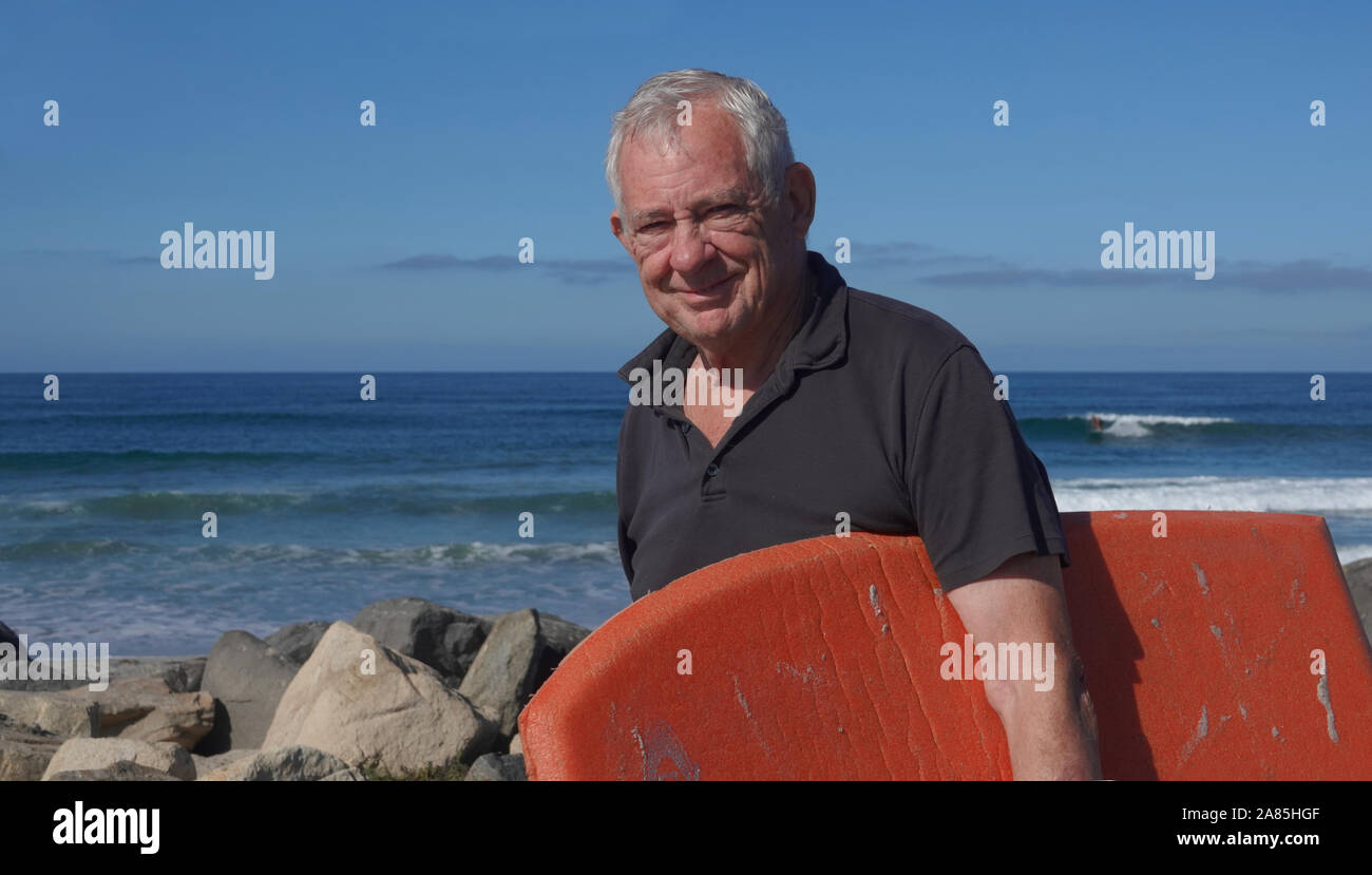 Happy, healthy, active octogenarian (80 year old Caucasian male) on the beach carrying his boogie board Stock Photo